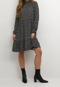 Vestito a righe bianche e nere con maniche lunghe, collo alto e orlo a strati. Indossato con stivali alla caviglia neri. Tessuto texturizzato con forme geometriche.