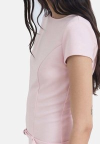 Haut ajusté rose avec manches courtes, encolure ronde et détails sur les coutures latérales. Le tissu semble lisse avec une légère brillance.