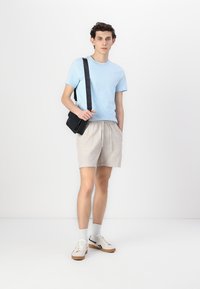 Ανοιχτό μπλε μπλουζάκι, μπεζ σόρτσ, μαύρη τσάντα μέσης, λευκά αθλητικά παπούτσια με καφέ σόλα, γκρι κάλτσες. Απλή, περιστασιακή εμφάνιση για ζεστό καιρό.