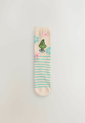 Knit socks with a beige base, featuring a green character design, pink and blue snowflake patterns, and turquoise stripes near the base.