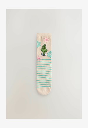 Knit socks with a beige base, featuring a green character design, pink and blue snowflake patterns, and turquoise stripes near the base.