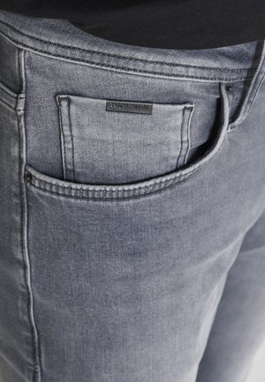 Dunkelgraue Jeans aus Denim mit strukturiertem Finish, ausgestattet mit einer Gesäßtasche und einem kleinen schwarzen Etikett, auf dem "ANTHONY MORATO" steht.