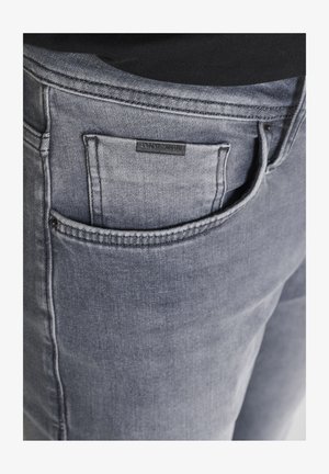 Jeans de mezclilla gris oscuro con un acabado texturizado, que presentan un bolsillo trasero y una pequeña etiqueta negra que dice "ANTHONY MORATO."
