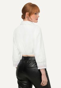 Weißes, kurzes Blusenshirt mit Spitzeneinsatz an den Ärmeln, klassischem Kragen und gerafftem Bund, kombiniert mit schwarzen Kunstlederhosen.