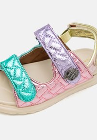 Kleurige sandaal met metallic roze, groene en paarse banden, met gestructureerde oppervlakken, voorzien van een decoratieve knop en een flexibele, beige zool.