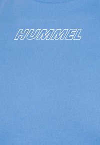 Tissu bleu respirant avec texte "HUMMEL" en blanc contouré, centré près du haut, indiquant une marque de vêtements de sport.