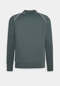 Donkergroene sweatshirt met een hoge hals, ribgebreide manchetten en zoom, een zachte textuur en witte piping langs de schoudernaden.