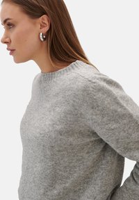 Szary sweter dzianinowy z okrągłym dekoltem, charakteryzujący się miękką teksturą i subtelnymi przebłyskami, w połączeniu z metalowymi kolczykami w kształcie obręczy.