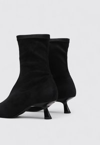 Black suede ankle boots with a slim stiletto heel and pointed toe. The design features a snug fit with smooth, textured fabric.