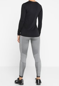 Top negro de manga larga combinado con leggings grises que presentan detalles de panel texturizado y un diseño ajustado, ideal para ropa deportiva.