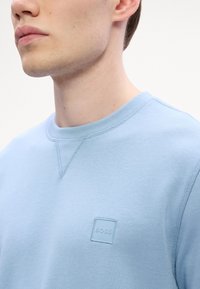 Ανοιχτό μπλε φούτερ από μαλακό ύφασμα, με στρογγυλή λαιμόκοψη και μικρό ανάγλυφο λογότυπο BOSS ραμμένο στο στήθος.