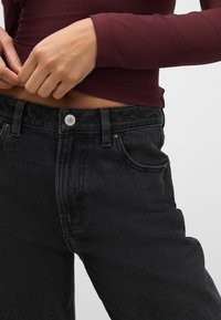 Zwarte denim jeans met een rechte snit, voorzien van een knoopsluiting, riemlussen en subtiele koperen klinknagels. Gladde textuur en minimalistisch ontwerp.