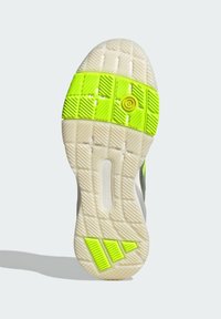 Shoe outsole featuring a textured, white rubber surface with bright green accents and a circular yellow detail at the center.