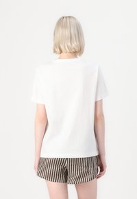 T-shirt en coton blanc avec un col rond et des manches courtes, vu de dos, associé à un short rayé beige et marron.
