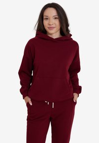 Burgundowa bluza z kapturem i kieszenią, luźny krój, kaptur ze sznurkiem, ściągacze na rękawach. W komplecie z dopasowanymi burgundowymi dresami. Gładka tekstura.