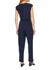 Marine jumpsuit met een soepele textuur, korte mouwen, elastische tailleband en een ritssluitingsdetail aan de achterkant. Uitlopers bij de benen, gecombineerd met zwarte hakken.