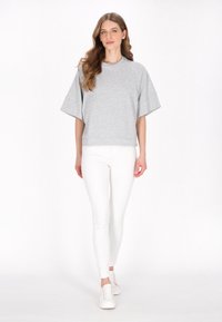 Felpa grigia a maniche corte oversize, in misto cotone, con scollo rotondo, abbinata a pantaloni bianchi slim-fit e sneakers bianche.