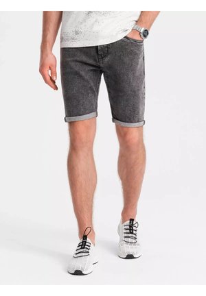 Sorte denimshorts med rullekanter, der har et klassisk fem-lomme design. Båret med hvide mesh sneakers, stående mod en neutral baggrund.