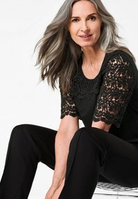 Zwart top met kantmouwen met florale patronen, gecombineerd met zwarte broek. De top heeft een ronde halslijn en een gestructureerd, ingewikkeld ontwerp.