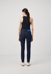 Námořnický tank top spárovaný s úzkými tmavými džíny s modrou nášivkou a viditelným šitím, doplněný bílými botami.