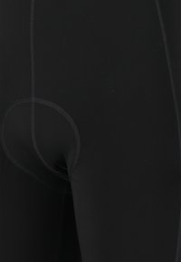 Leggings noirs en matériau extensible, dotés d'une texture lisse, de coutures visibles et d'un détail en forme de découpe circulaire au dos.