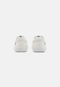Sneakers bianchi con una parte superiore in pelle liscia, punta arrotondata, suola piatta bianca e accenti di branding discreti sui lati e sul retro.