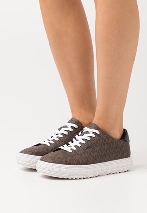 Brown patterned sneakers with white laces, textured fabric upper, black accents on the heel, and white rubber sole with a serrated edge.
