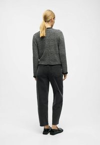 Schwarzer und weißer gemusterter Pullover mit rundem Halsausschnitt, kombiniert mit dunkelgrauen Hosen und glänzenden schwarzen Schuhen. Einfaches, strukturiertes Design.