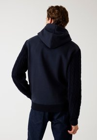Felpa navy con design a treccia su maniche, corpo in tinta unita e orlo a costine. Presenta un cappuccio e una vestibilità casual.