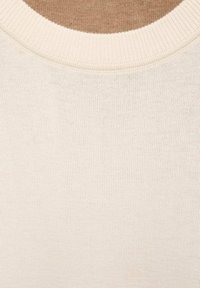 Gros plan sur le col d'un pull en laine de couleur crème avec une texture côtelée fine, mettant en valeur les détails du tissu et la couture.