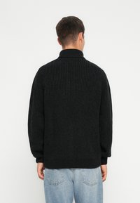 Svart strikkegenser med høy krage, med en teksturert vev og ribbede mansjetter, kombinert med lyseblå jeans.