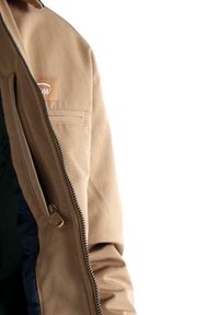 Primer plano de una persona que lleva una chaqueta color beige con una cremallera parcialmente abierta, mostrando una capa interna negra debajo.