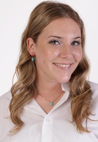Gouden ketting met een turquoise hanger, gecombineerd met bijpassende turquoise oorknoppen. Model draagt een witte button-up blouse.
