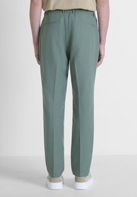 Pantaloni verdi a vestibilità comoda, con una vita elastica, due tasche posteriori e una texture liscia. Indossati con sneakers bianche.