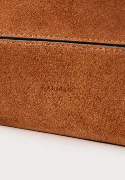Surface en cuir suédé marron avec des coutures visibles et le texte embossé "WANDLER" au centre sur un fond plat et clair.