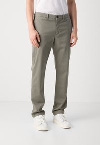 Khaki chinos, wykonane z lekkiego materiału, z prostym krojem, dwiema bocznymi kieszeniami, z guzikiem oraz noszone z białymi trampkami.