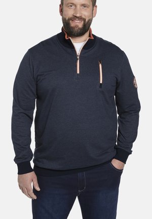 Dunkelblauer Pullover mit hohem Kragen, orangefarbenen Akzenten und einer mit Reißverschluss versehenen Brusttasche. Rippbündchen und Saum. Weicher, strukturiert Stoff.
