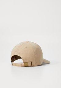 Beige Baumwoll-Basketballmütze mit gebogenem Schirm, einstellbarem Metallstrap in Goldfarbe und genähten Belüftungslöchern auf der Rückseite.
