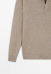 Beige strikket sweater med lange ærmer, ribbede manchetter og kant samt en V-formet halsudskæring på en hvid baggrund.