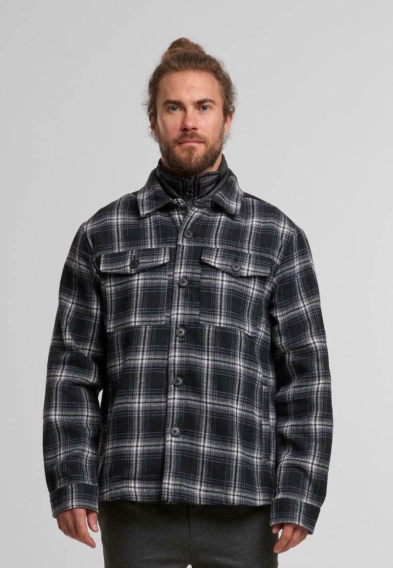 Schwarze und weiße kariierte Flanelljacke mit Knopfverschluss, zwei Brusttaschen und hohem Kragen. Die Textur wirkt weich und warm.