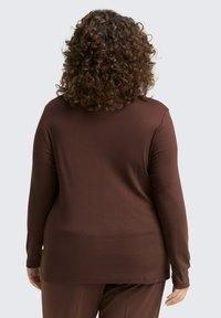Langarmtop van bruine stof, met een ontspannen pasvorm en een eenvoudig ontwerp. Glad textuur met een rechte zoom en lange mouwen.