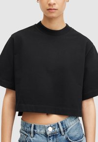 Melnā īsā krekla ar īsām piedurknēm, izgatavota no kokvilnas. Tam ir apaļa kakla izgriezuma forma un taisna apakšmala, valkāta ar augsto jostasvietu džinsa īsu biksēm.