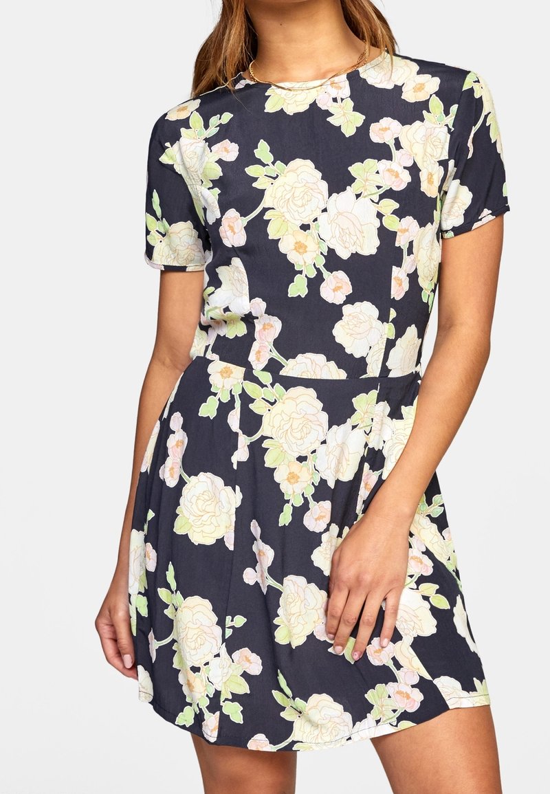 Robe à motif floral avec manches courtes, corsage ajusté et jupe évasée. Fond bleu marine avec des accents de fleurs blanches et vertes.