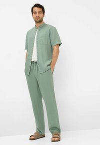 Light green linen short-sleeve shirt with buttons, pocket, and matching loose-fit pants. Worn with brown strappy sandals.