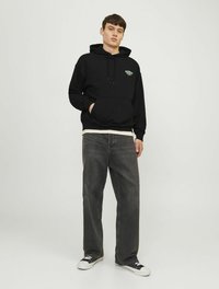 Czarna bluza z kapturem z kieszenią kangurką, z kolorowym logo. Połączona z szarymi spodniami wide-leg i czarnymi sneakersami z białymi akcentami.