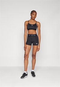 Zwart sportief crop top met dunne banden en logo, gecombineerd met bijpassende zwarte shorts. Draag met zwarte hardloopschoenen en witte sokken.