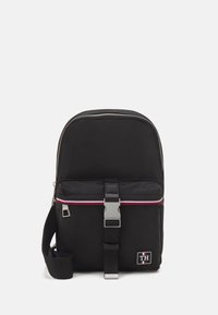Zaino in nylon nero con una parte superiore arrotondata, zip argentata, striscia orizzontale rossa e bianca, tracolla regolabile e tasca frontale con una chiusura in metallo.