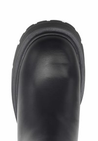 Botín de cuero negro con punta redondeada, acabado texturizado y una suela de goma gruesa con ranuras horizontales para tracción.