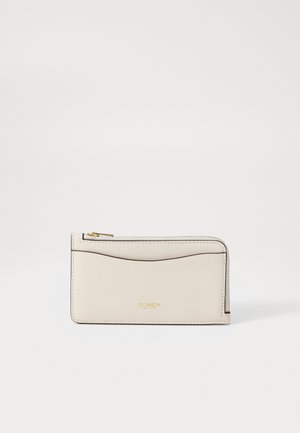Light beige leather wallet with gold hardware, smooth texture, zip closure, and a curved design detail on the front. Brand logo visible.