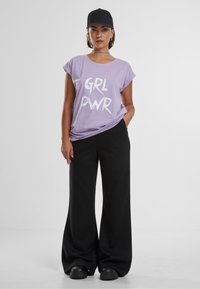 Lilla oversized t-shirt med "GRL PWR" grafik, парен med brede sorte bukser og en sort kasket. Blødt stof, afslappet pasform.